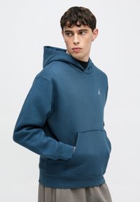 Φούτερ με κουκούλα σε σκούρο μπλε βαμβακερό μείγμα, με μπροστινή τσέπη και λευκό λογότυπο. Λεία υφή με μανσέτες και τελείωμα με ριμπ ύφανση.