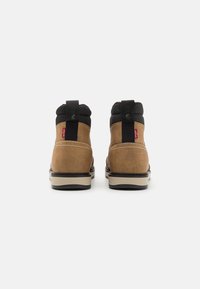 Hnědé semišové kotníkové boty s černým polstrovaným límcem, mají texturovanou gumovou podrážku a červenou cedulku Levi's na patě.