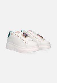 Zapatillas de cuero blancas con una suela gruesa blanca, con acentos verdes en el talón y joyería decorativa en los cordones.