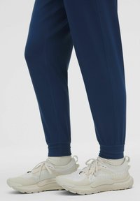 Bílé a béžové sportovní boty s texturovanými akcenty, spárované s námořnickým joggerem s elastickými manžetami. Měkké pletené ponožky viditelné nad botami.