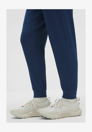 White and beige athletic shoes with textured accents, paired with navy joggers featuring elastic cuffs. Soft knit socks visible above shoes.