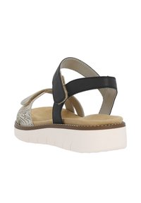 Sandales noires et beiges avec un dessus à motifs, des sangles ajustables et une semelle blanche rembourrée. Présentent un talon plat et une semelle intérieure texturée.