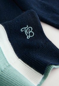 Puuvillasegu sokid, millel on tumesinised, helesinised ja valged triibud. Heledas sinises brodeeritud "TB" logo. Ühtlane kootud muster üle kogu sokki.