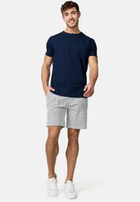 Camisa henley de manga corta en azul marino combinada con pantalones cortos blancos con un diseño geométrico, complementada con zapatillas blancas.