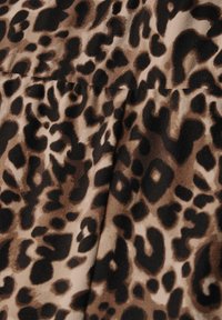 Tessuto a stampa leopardata in tonalità di beige e marrone, con una texture liscia e macchie nere irregolari di forme diverse.
