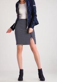 Navy jacket with a slim fit, paired with a striped pencil skirt featuring a side zip, worn with black ankle boots.