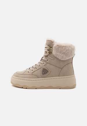 Stivale sneaker beige high-top con suola spessa, chiusura con lacci, occhielli dorati, collo in pelliccia sintetica e toppa decorativa sul lato.