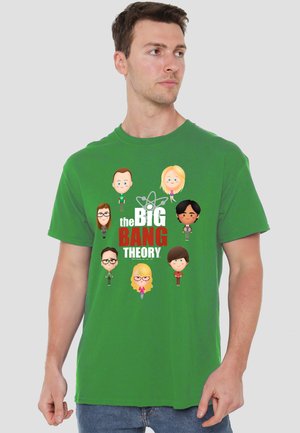 Man wearing green T-shirt with cartoon faces of seven characters and "The Big Bang Theory" text in white and red.