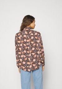 Blusa floral con base negra, que presenta patrones de flores naranjas y rosas. Mangas largas, con puños, y un corte relajado.
