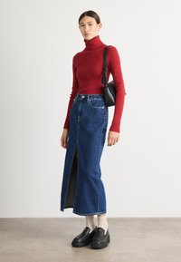 Rdeča rebrasta turtleneck pulover, dolga modra denim krilo s sprednjim razporkom, v kombinaciji s črnimi čevlji na drsanje in belimi crew nogavicami. Črna torba.