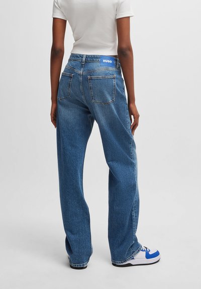 Jean en denim bleu à jambes larges et taille haute, avec une étiquette "HUGO" bleue, deux poches arrière et des ourlets bruts pour un look décontracté.