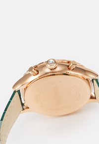 Orologio da polso per donna in acciaio inossidabile dorato con cinturino in pelle verde. Presenta una cassa rotonda e una corona laterale con un accento di cristallo.