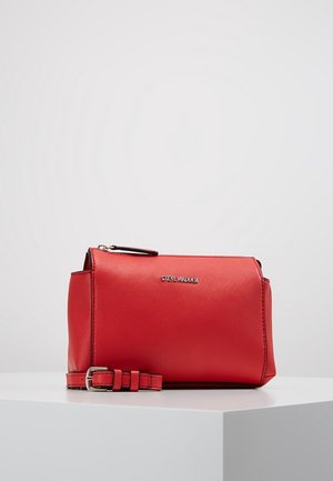 Petit sac bandoulière en cuir rouge avec boucle et fermeture éclair argentées, logo Steve Madden à l’avant, présenté sur une surface blanche.