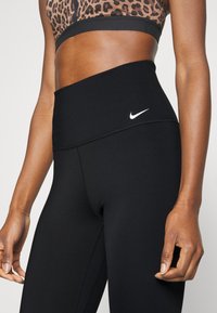 Leggings negros de cintura alta con una textura suave y detalles cosidos, con un pequeño logo blanco de Nike en la cintura.