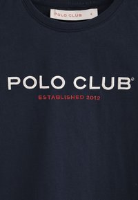 Camiseta de algodón azul marino con cuello redondo, que presenta texto bordado en blanco y rojo "POLO CLUB" y "ESTABLECIDO 2012" debajo.