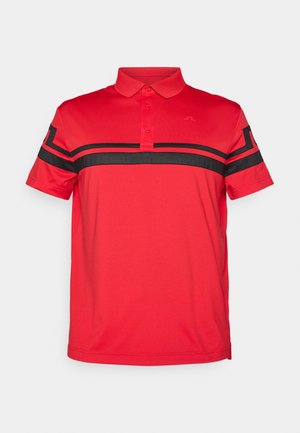 Sarkana polo krekls, kas izgatavots no gludas auduma, ar melnu horizontālu svītru pār krūtīm un īsām piedurknēm. Divu pogu apkakles dizains.