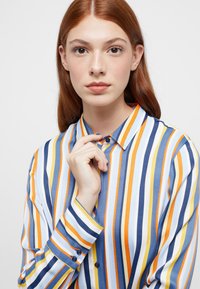 Button-up shirt with vertical stripes in yellow, orange, blue, and white. Features a standard collar and button cuffs. Smooth fabric texture.