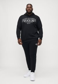 Schwarzer Kapuzenpullover und passende Jogginghose aus weichem Stoff, mit einem auffälligen Logo in Weiß. Akzentuiert mit verstellbarer Kapuze und Bündchen.