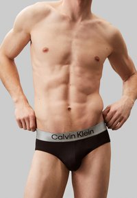 Schwarze Baumwollslips mit einem grauen elastischen Bund, der mit "Calvin Klein"-Markierung versehen ist. Designed mit einer figurbetonten Form und glatter Textur.