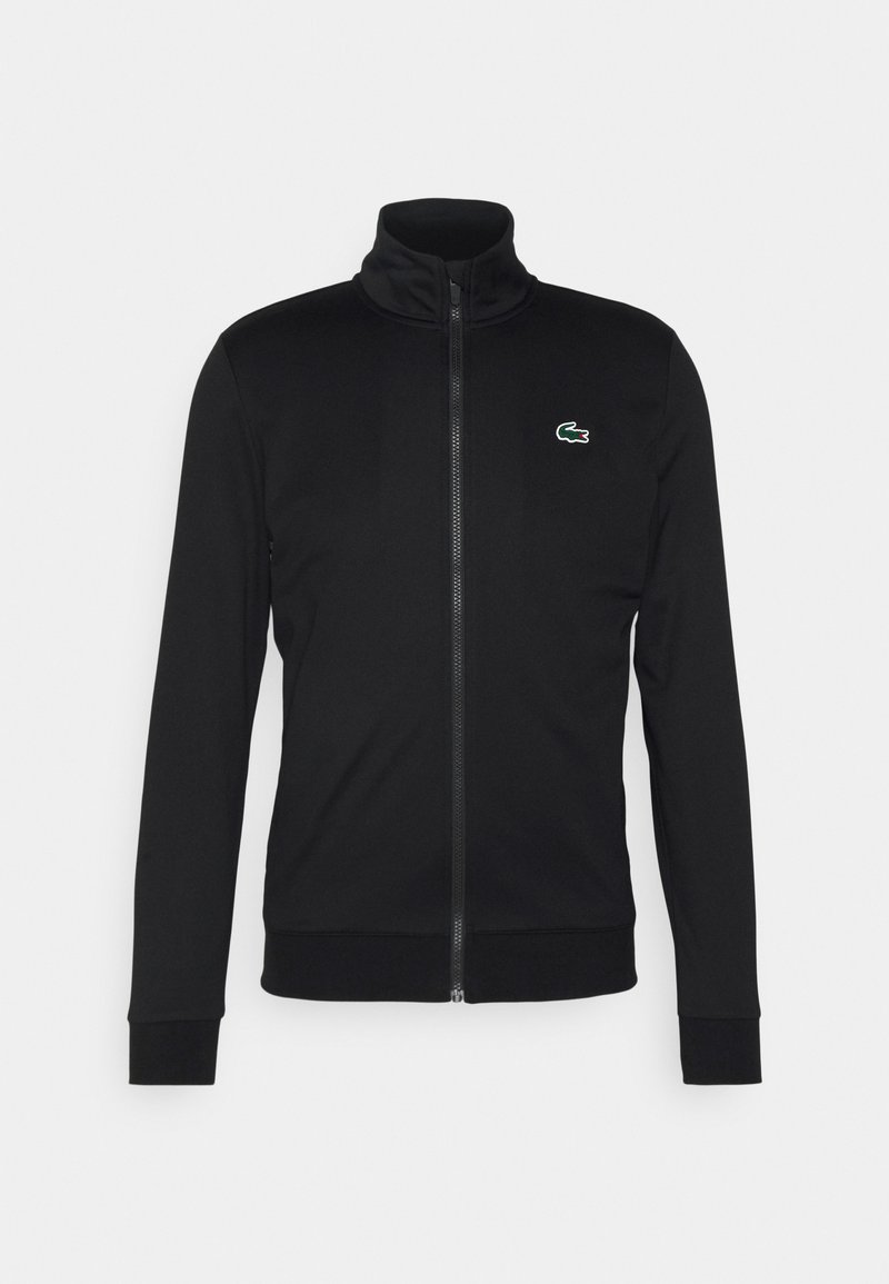 Zwarte zip-up jas met hoge kraag, gemaakt van een gladde stof. Kenmerkt zich door een klein groen Lacoste-logo op de linkerborst en geribde manchetten.