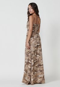 Maxi dress in brown tones with a nature-inspired pattern, featuring thin adjustable straps and a fitted bodice with a flowy skirt.