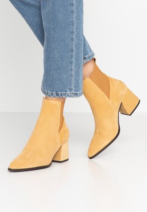 Stivaletti alla caviglia gialli in suede con punta affusolata, tacco a blocco e pannelli elastici laterali, abbinati a jeans azzurri a gamba dritta.