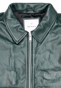 Giacca di pelle verde con chiusura a zip, texture liscia e colletto classico. Presenta un'etichetta bianca interna con testo stampato.