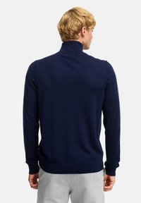 Maglione lavorato a maglia blu navy con colletto alto, maniche lunghe e polsini e orlo a coste. Texture morbida, design semplice e silhouette aderente.