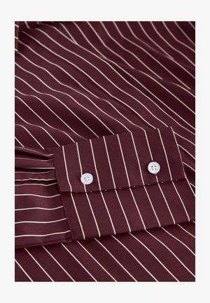 Burgundy shirt with white vertical stripes, featuring a buttoned cuff and a smooth fabric texture. Double button closure with tonal stitching.