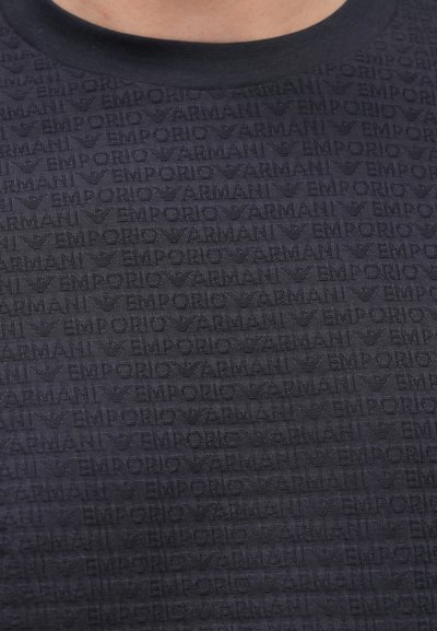 Tmavomodré tričko so štruktúrovaným vzorom opakujúceho sa loga "Emporio Armani" a dizajnom orla. Okrúhly výstrih, krátke rukávy.