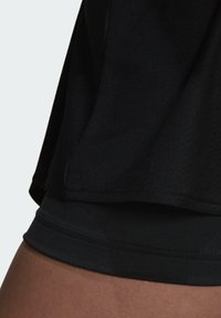 Top atlético negro con una textura suave, mangas cortas y un dobladillo redondeado. El diseño es ajustado, con un acabado sin costuras en los bordes.