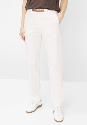 Hvide bukser med lige ben og sidelommer, båret med et brunt bælte, en mørkebrun top og hvide sneakers med gummisåler.