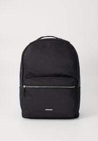 Mochila negra hecha de tela duradera, con una superficie suave, diseño redondeado, un bolsillo frontal con cremallera y un acento plateado minimalista.
