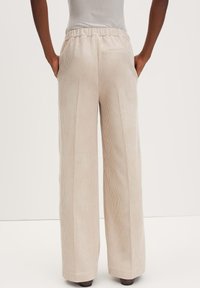 Beige brede corduroy broek met een zachte textuur, elastische tailleband en één achterzak. Het verticale ribpatroon versterkt het ontwerp.