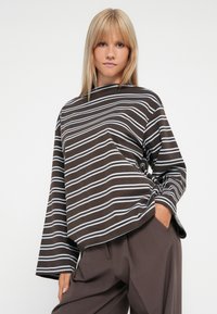 Loose-fitting brown top featuring horizontal blue stripes, round neck, and wide sleeves. Paired with relaxed-fit brown trousers.