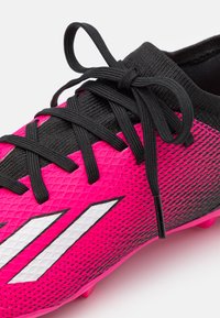 Scarpa da calcio rosa e nera con tomaia texturizzata, lacci neri e accenti di branding bianchi, con suola sagomata per la trazione.