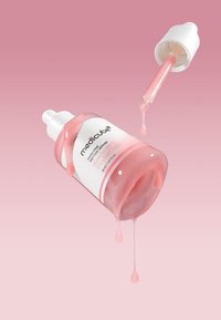 Bottiglia di siero rosa con tappo contagocce; un liquido goccia a goccia esce dalla bottiglia, che presenta un'etichetta bianca e una finitura liscia e lucida.