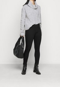 Šedý pletený svetr s lodičkovým výstřihem, černé úzké kalhoty a černé kotníkové boty, doplněné černou koženou kabelkou.