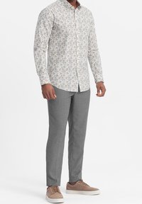 Lange mouwen knoop blouse in een lichte kleur met bloemmotief, gecombineerd met grijze textuurbroek en bruine sneakers.