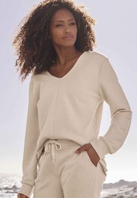 Maglia beige a maniche lunghe con collo a girocollo e texture a coste abbinata a pantaloni con coulisse coordinati; entrambi presentano una vestibilità comoda e tasche laterali.