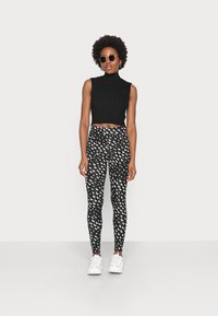 Top cropped sem mangas, com nervuras pretas, combinado com leggings pretas com um padrão de lua crescente branca, finalizado com ténis brancos e óculos de sol.