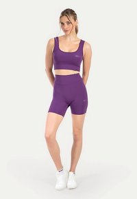 Paarse sportieve cropped top en hooggetailleerde shorts, gemaakt van rekbaar materiaal met een gladde textuur. Voorzien van minimale merkaccenten.