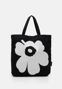 Black tote bag featuring a large white flower design with a black center. Made of fabric with two sturdy black handles.