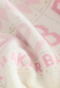Tejido de punto suave en blanco y rosa con letras y bordados de pequeñas estrellas doradas, mostrando un primer plano de la textura y los pliegues.