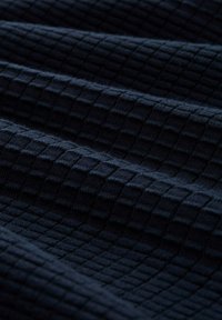 Teksturowany ciemnoniebieski materiał z wzorem w kratkę, z wystającymi kwadratami i miękką, puszystą fakturą, złożony w taki sposób, aby ukazać głębię i wymiar.