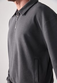Maglione grigio con design a maglia a cialda testurizzato, dotato di collo con zip e tasche laterali per una maggiore funzionalità.