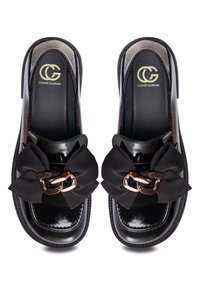 Mocassins noirs brillants avec grands nœuds en tissu noir et détail chaîne dorée à l'avant, marqués Cesare Gaspari à l'intérieur.