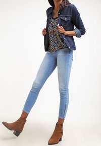 Chaqueta vaquera, top floral, vaqueros pitillo azul claro con cremalleras en los tobillos y botines marrones.