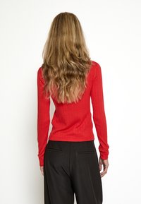 Top de manga larga rojo con diseño ajustado, que presenta un escote redondo y acentos minimalistas. Combinado con pantalones negros.