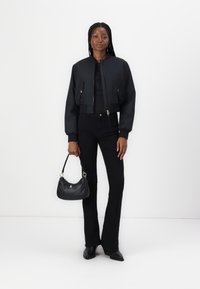 Afgeknotte zwarte bomberjack met een ritssluiting aan de voorkant, twee klepzakken, gecombineerd met zwarte flare pants en een kleine zwarte handtas.